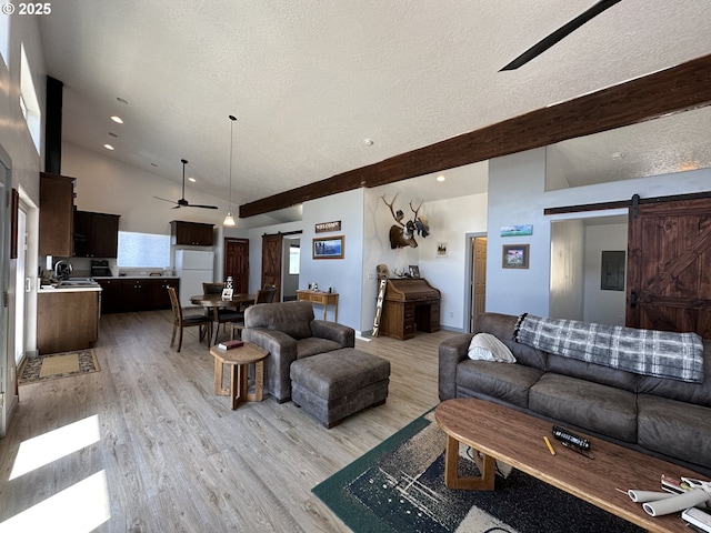 living area with a barn door, a textured ceiling, light wood-style flooring, a ceiling fan, and vaulted ceiling with beams