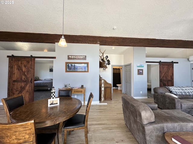 dining space with baseboards, a barn door, light wood finished floors, and beam ceiling