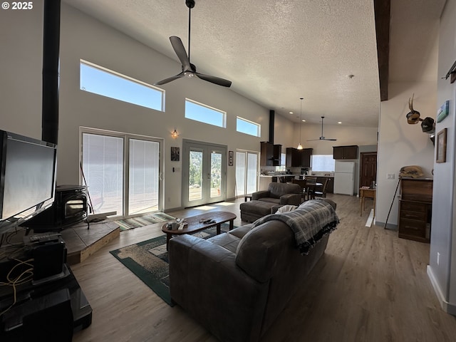 living area with a textured ceiling, ceiling fan, light wood finished floors, and a towering ceiling