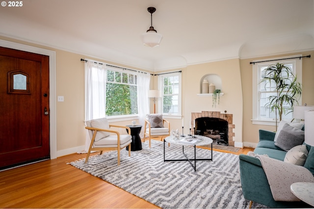 living room with a brick fireplace, crown molding, and light wood-type flooring