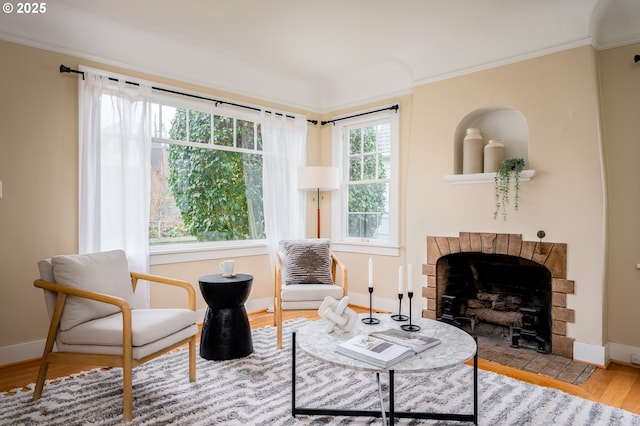 living area featuring a healthy amount of sunlight, a fireplace, ornamental molding, and light hardwood / wood-style floors