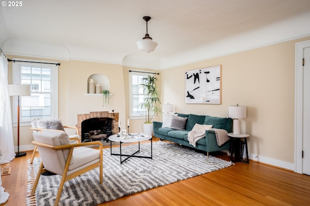 living room featuring a brick fireplace, plenty of natural light, wood-type flooring, and ornamental molding