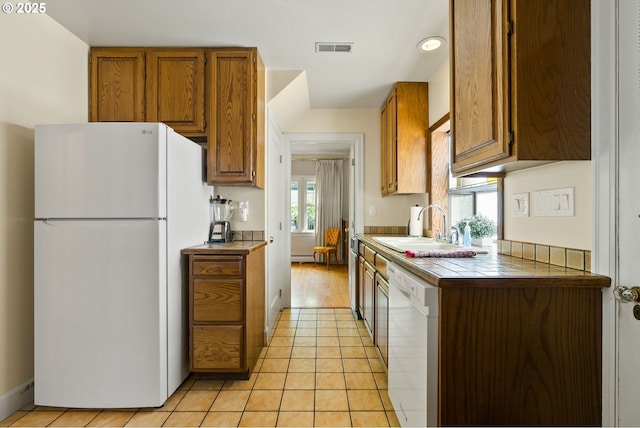 kitchen featuring white appliances, a sink, tile counters, brown cabinetry, and recessed lighting