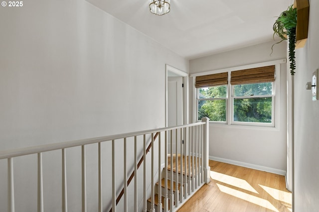 hall with wood finished floors, an upstairs landing, and baseboards