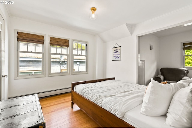 bedroom with light wood finished floors, ornamental molding, and a baseboard heating unit