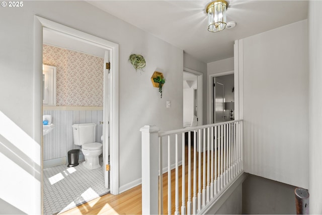 hall featuring wallpapered walls, an upstairs landing, baseboards, and wood finished floors