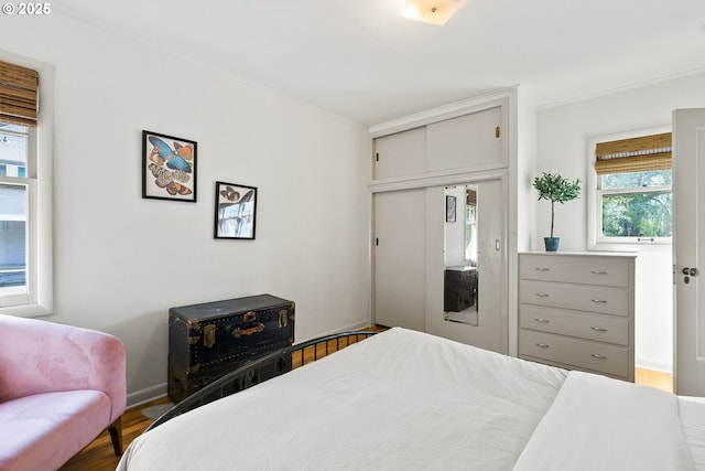 bedroom with a closet, wood finished floors, baseboards, and ornamental molding