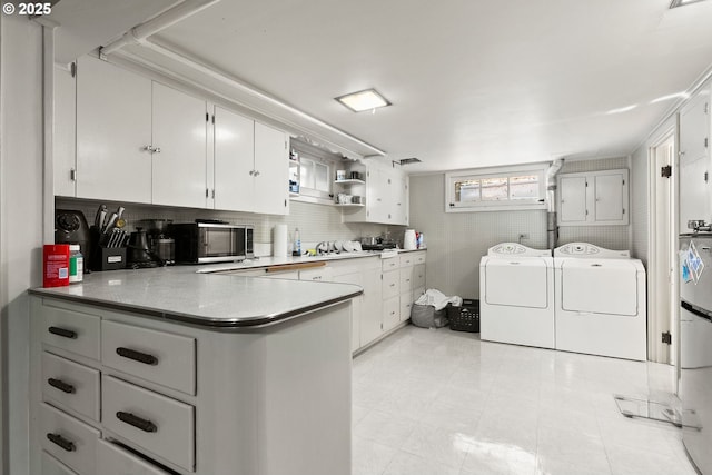 kitchen featuring washing machine and dryer, stainless steel microwave, a peninsula, open shelves, and white cabinetry