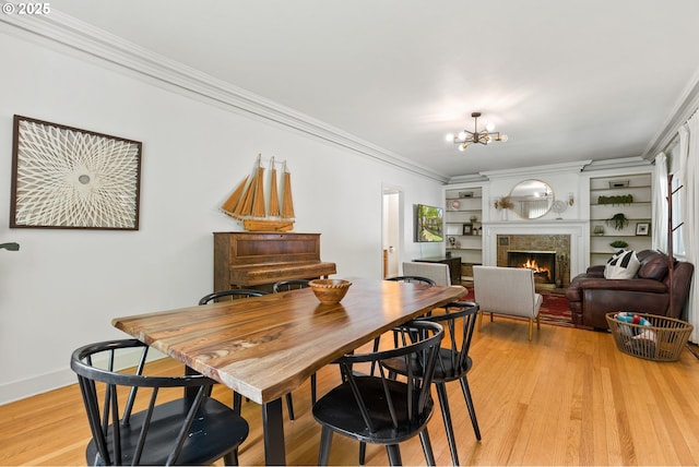 dining space with ornamental molding, a chandelier, a tiled fireplace, light wood finished floors, and baseboards