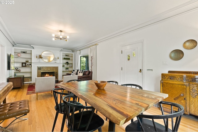 dining room with ornamental molding, light wood-style flooring, a chandelier, and a tile fireplace