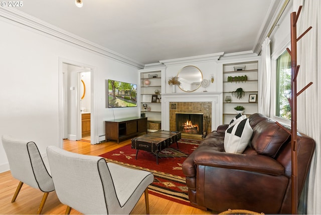 living area with ornamental molding, light wood-style floors, a tile fireplace, baseboards, and built in shelves