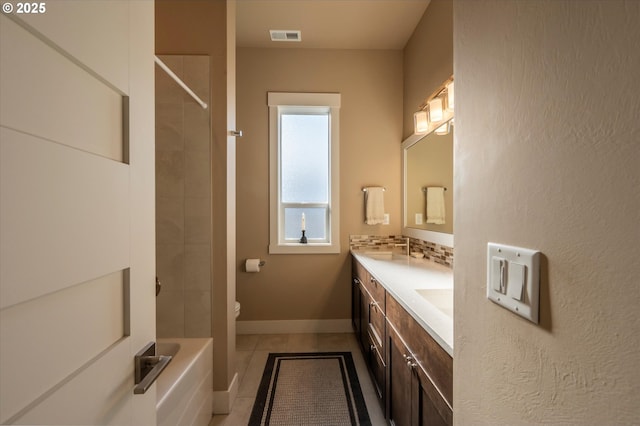 bathroom featuring tile patterned flooring, backsplash, vanity, a tile shower, and toilet