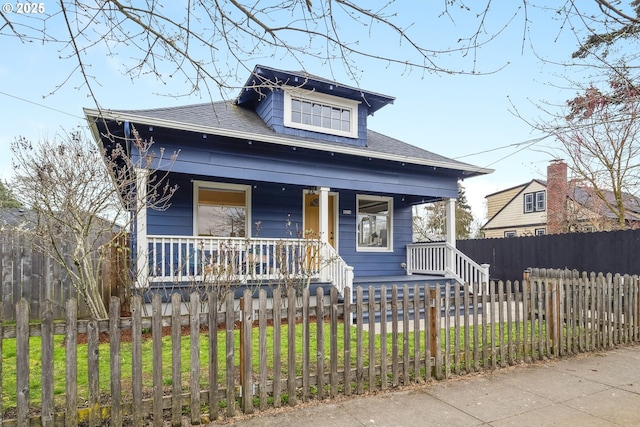 bungalow with a fenced front yard, roof with shingles, a porch, and a front lawn