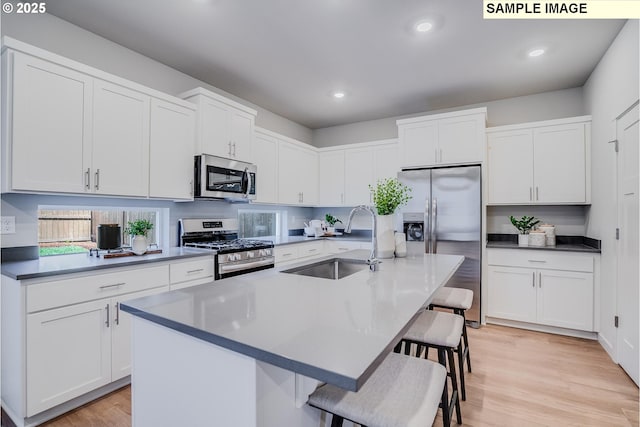 kitchen with sink, a breakfast bar area, a kitchen island with sink, stainless steel appliances, and white cabinets