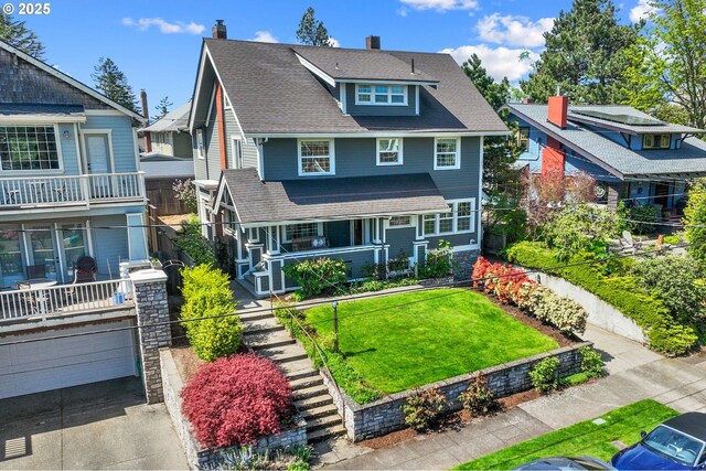 american foursquare style home featuring covered porch, an attached garage, a chimney, a shingled roof, and a front yard