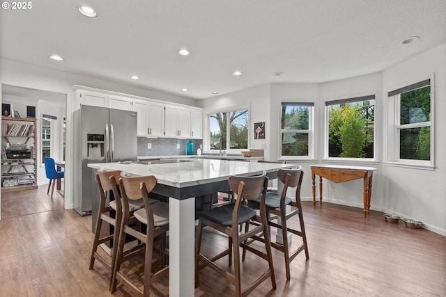 kitchen with white cabinetry, a kitchen bar, decorative backsplash, stainless steel fridge, and a kitchen island