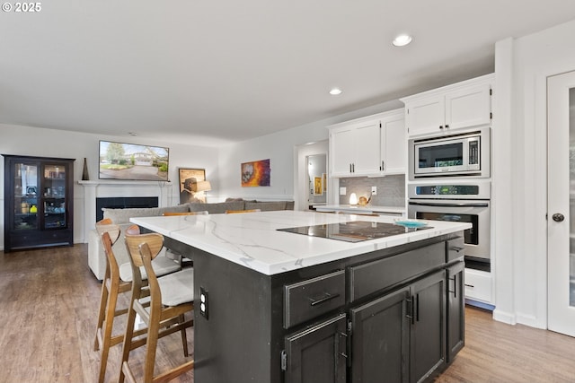 kitchen featuring white cabinets, a center island, light hardwood / wood-style flooring, backsplash, and appliances with stainless steel finishes