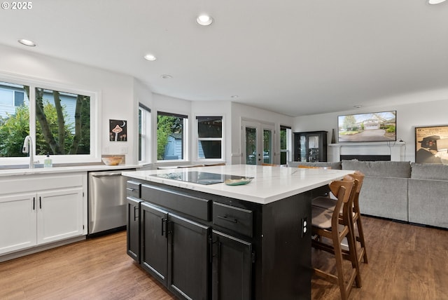 kitchen featuring dishwasher, black electric cooktop, a kitchen island, a kitchen breakfast bar, and sink