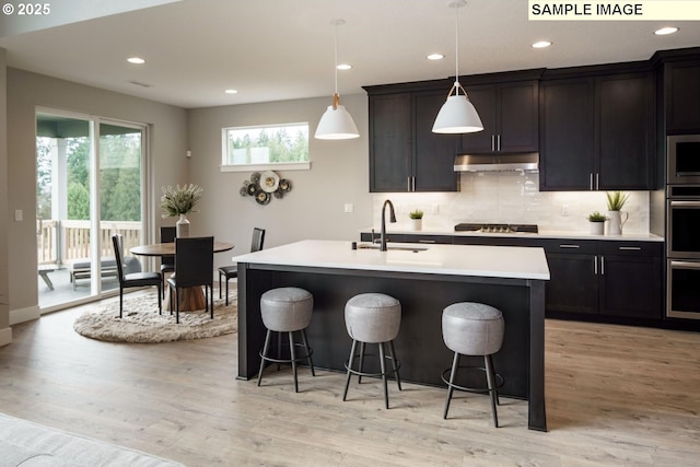 kitchen featuring sink, decorative light fixtures, a center island with sink, light hardwood / wood-style flooring, and a wealth of natural light