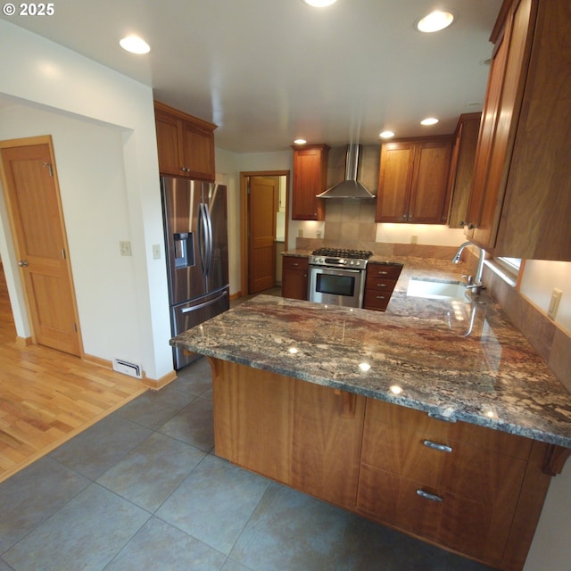 kitchen featuring stainless steel appliances, wall chimney range hood, a sink, brown cabinets, and recessed lighting