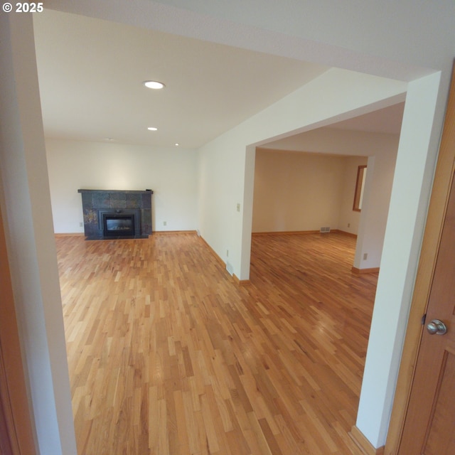 unfurnished living room with light wood-type flooring, a glass covered fireplace, recessed lighting, and baseboards