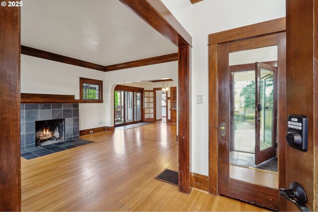 foyer with a tile fireplace, wood-type flooring, and ornamental molding