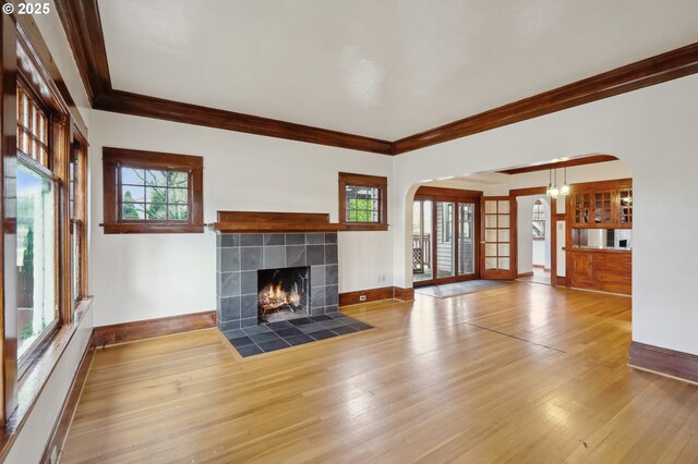 unfurnished living room featuring hardwood / wood-style floors, crown molding, a fireplace, and french doors