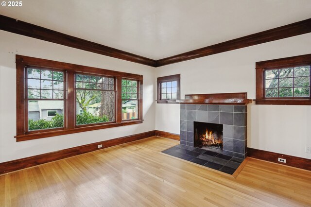 unfurnished living room with a tile fireplace, ornamental molding, hardwood / wood-style flooring, and a healthy amount of sunlight