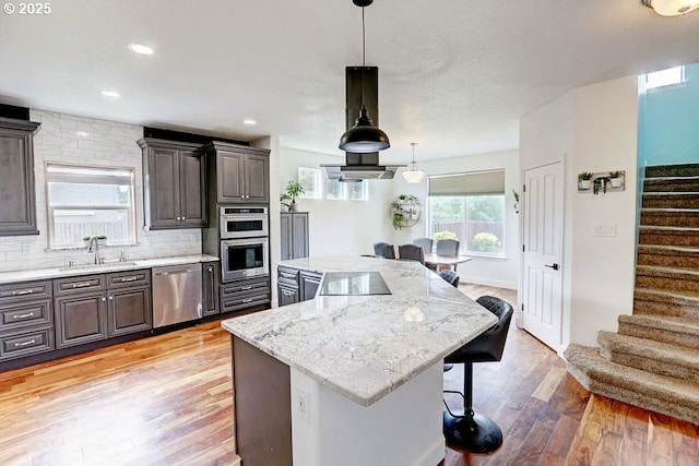 16295 SE Slate St, Damascus, OR 97089 - kitchen featuring appliances with stainless steel finishes, a sink, a center island, a kitchen bar, and light wood-style floors