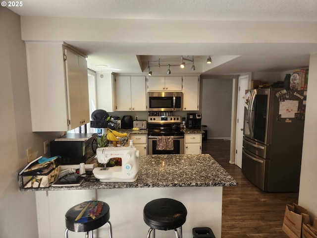 6307 NE Wilding Rd, Vancouver, WA 98686 - kitchen featuring appliances with stainless steel finishes, a peninsula, dark wood-style flooring, dark stone countertops, and white cabinetry