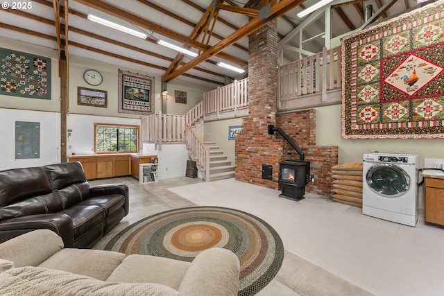 living room featuring high vaulted ceiling, washer / clothes dryer, a wood stove, and stairs