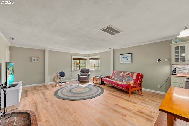 living room featuring ornamental molding, light wood-type flooring, visible vents, and baseboards