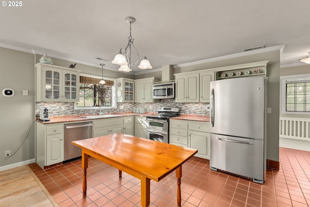 kitchen featuring light countertops, decorative backsplash, appliances with stainless steel finishes, ornamental molding, and a sink