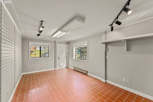 tiled empty room featuring crown molding, baseboard heating, rail lighting, and a healthy amount of sunlight