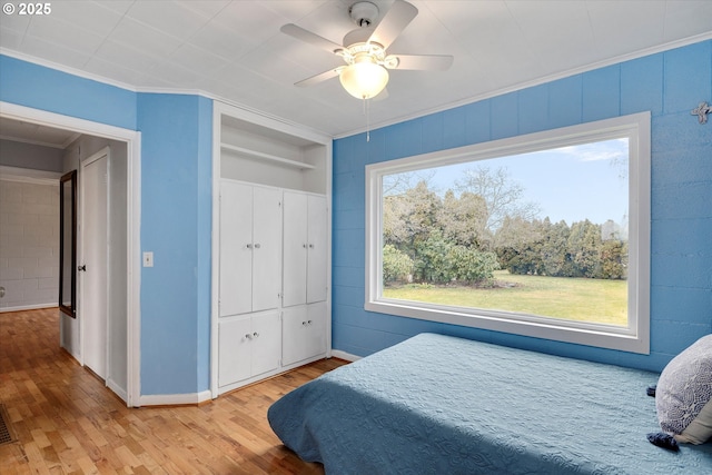 bedroom with a closet, ornamental molding, ceiling fan, wood finished floors, and baseboards