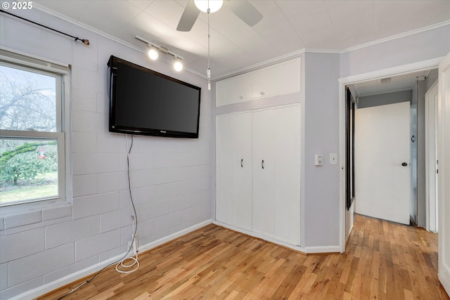 unfurnished bedroom featuring ornamental molding, concrete block wall, multiple windows, and light wood finished floors