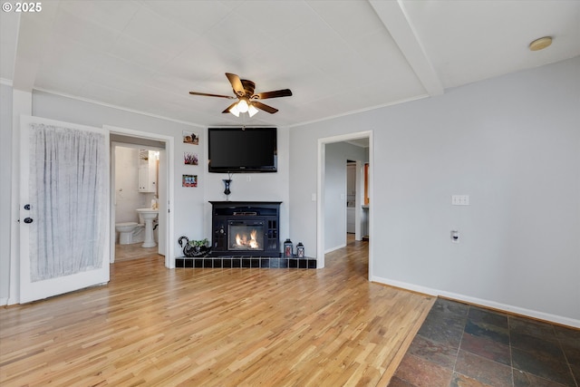 living room featuring baseboards, a tile fireplace, ceiling fan, wood finished floors, and crown molding