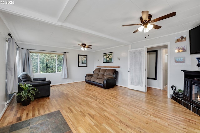 living room with baseboards, crown molding, a tiled fireplace, and light wood-style floors