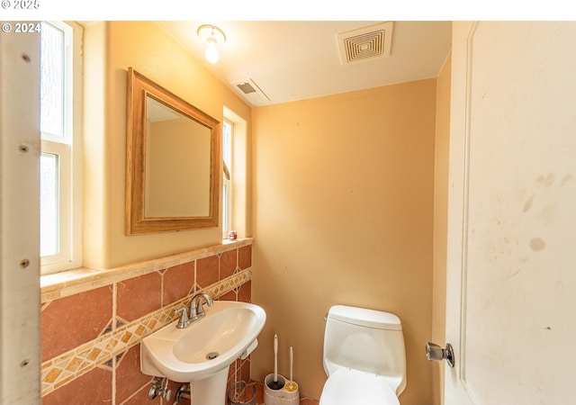 half bathroom featuring visible vents, a sink, backsplash, and toilet