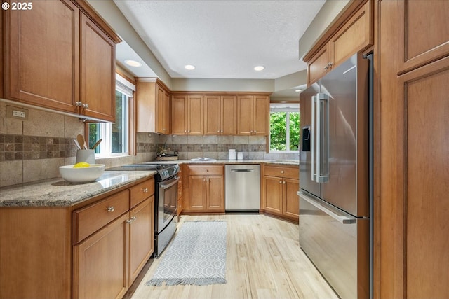 17221 SW Oakenshield Ct, Portland, OR 97224 - kitchen featuring appliances with stainless steel finishes, light wood-style flooring, brown cabinetry, light stone counters, and backsplash