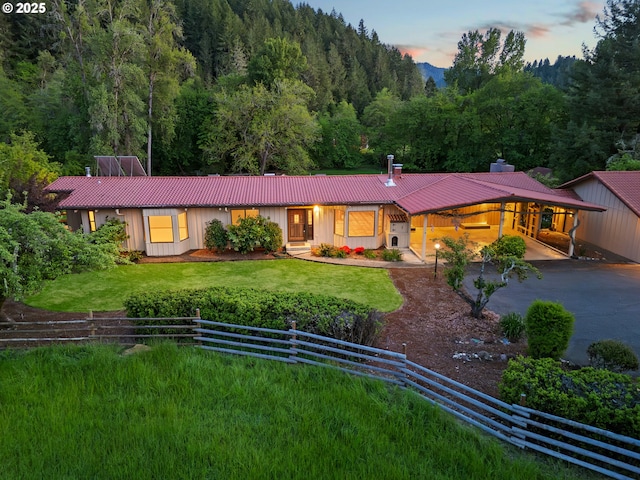 view of front facade with fence, a front lawn, a chimney, a forest view, and metal roof