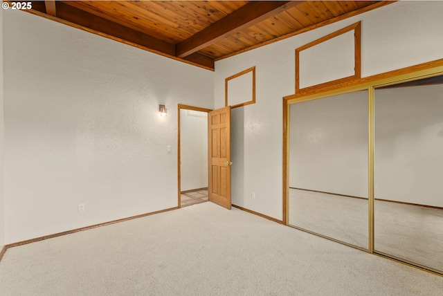 unfurnished bedroom featuring light carpet, baseboards, beamed ceiling, wood ceiling, and a closet