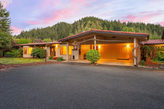view of front facade featuring a wooded view, driveway, and an attached carport