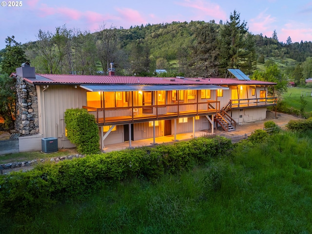 rear view of house with a wooden deck, a chimney, metal roof, central air condition unit, and a wooded view