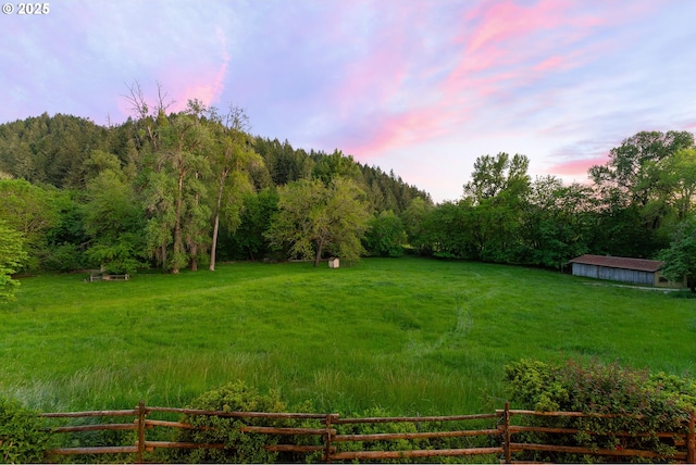 yard at dusk featuring fence, a rural view, and a forest view