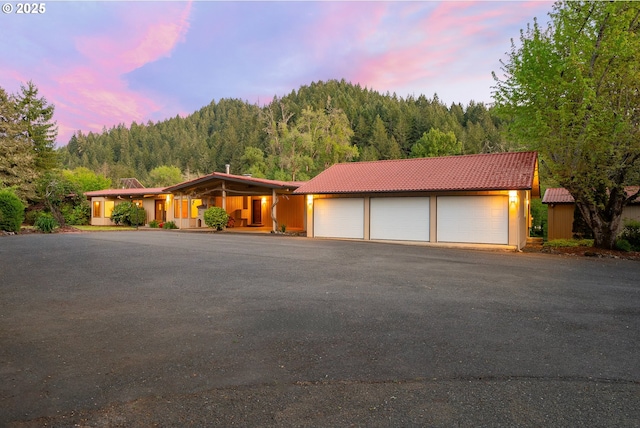 view of front of property with a garage, a tiled roof, a wooded view, and covered porch
