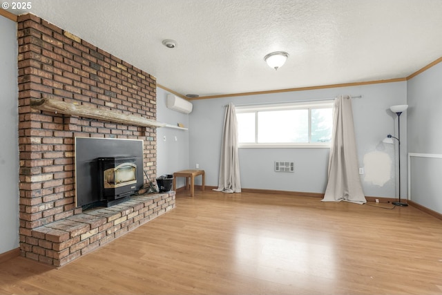 unfurnished living room with a wall mounted AC, a textured ceiling, a wood stove, light wood-type flooring, and ornamental molding