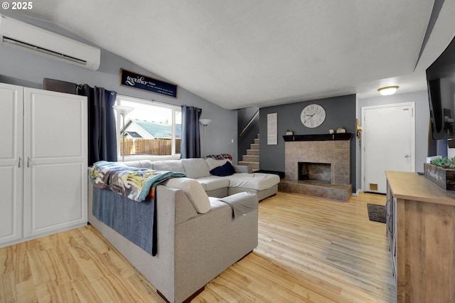 living room with a tiled fireplace, lofted ceiling, light hardwood / wood-style flooring, and a wall mounted air conditioner