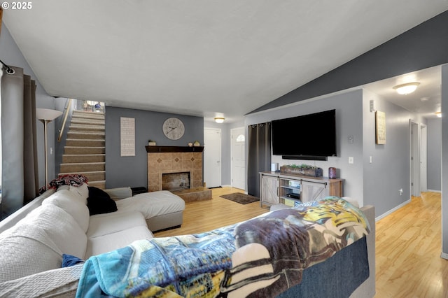 living room with a tile fireplace, light wood-type flooring, and vaulted ceiling