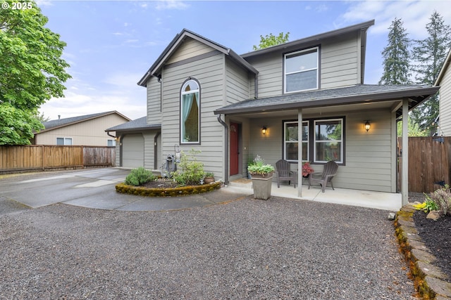 traditional-style home featuring a garage, fence, roof with shingles, concrete driveway, and a porch